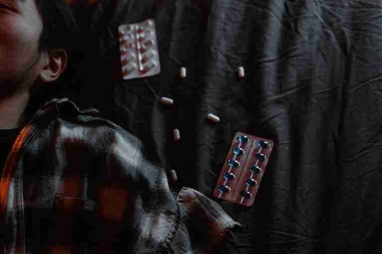 Moody portrait of a man lying next to scattered tablets, expressing distress.