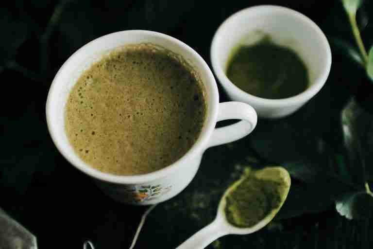 Close-up of a frothy matcha latte in a ceramic cup with matcha powder on spoon.