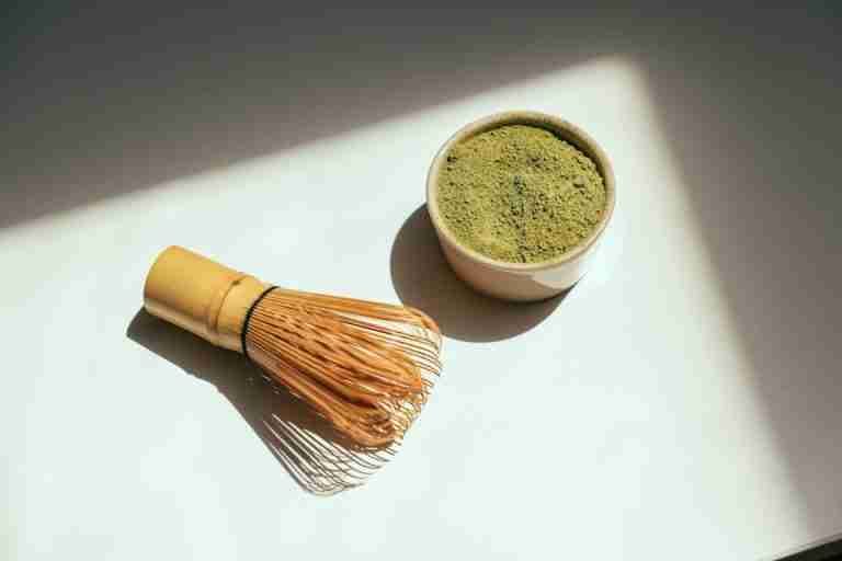 Minimalist composition featuring matcha powder and bamboo whisk in sunlight.