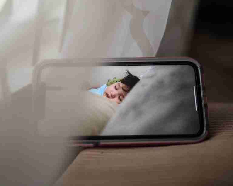 A smartphone displaying a sleeping baby in a cozy, indoor setting, conveying warmth and care.