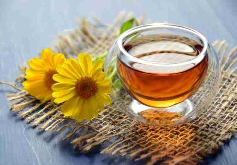 Glass cup of herbal tea with yellow flowers on a textured background.