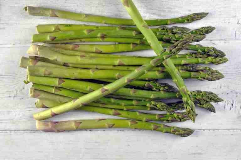 A vibrant bunch of green asparagus spears laid out on a white wooden surface, showcasing fresh produce.