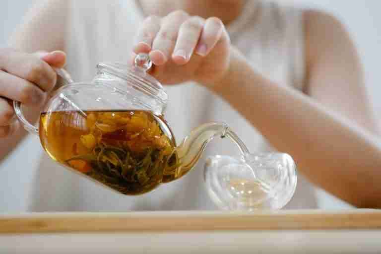 Adult woman pouring herbal tea into a cup, showcasing a cozy indoor tea ritual.