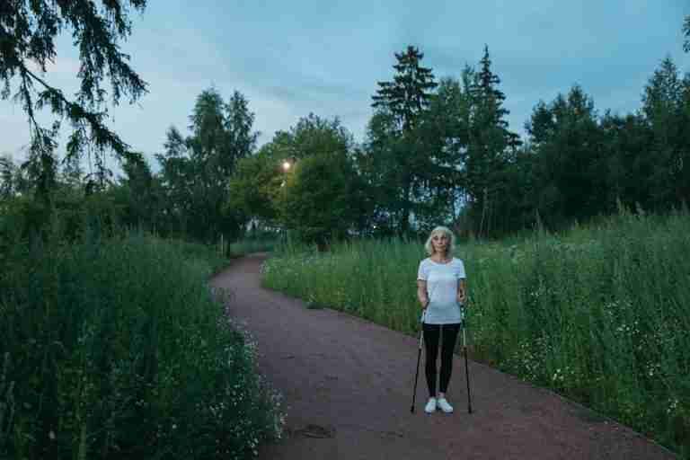 Senior woman exercising with Nordic walking poles in a peaceful green park during daytime.