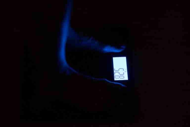 Close-up of a digital weighing scale displaying weight in a dark room with blue illumination.