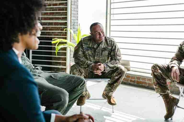 A group therapy session with military personnel discussing mental health support in a bright room.