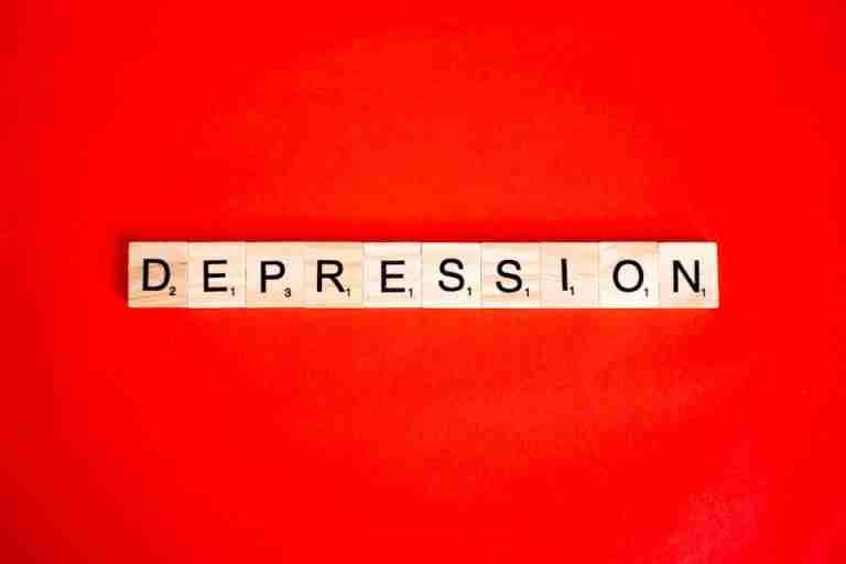 Word depression spelled with letter tiles on vibrant red background, highlighting mental health theme.