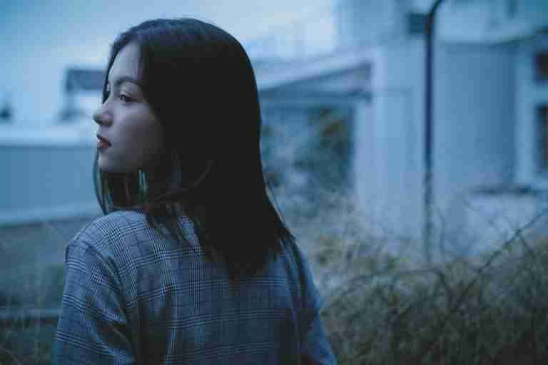 A reflective teenage girl gazes thoughtfully in a quiet urban environment during twilight.