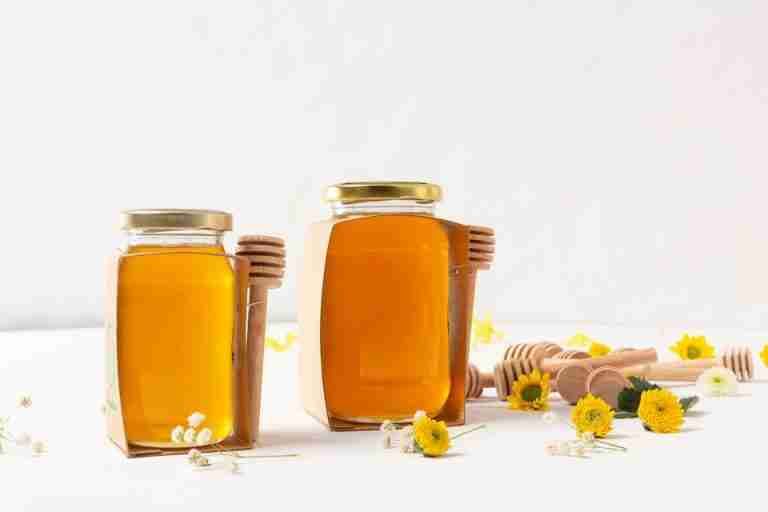 Aesthetic portrayal of honey jars with dippers and flowers on a white background.