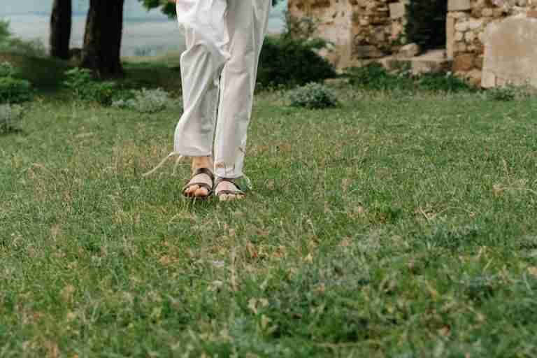 A person walking on green grass wearing white pants and sandals, a relaxed outdoor scene.