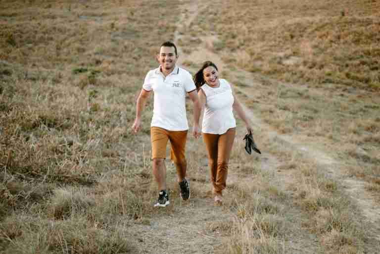 Joyful couple holding hands and walking through a grassy field, enjoying a sunny day.