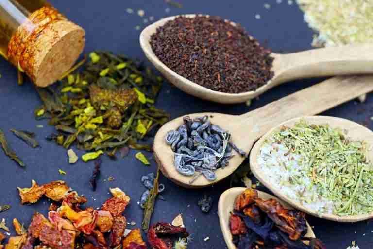 Assorted loose leaf herbal teas in wooden spoons on a flat lay composition, showcasing various colors and textures.