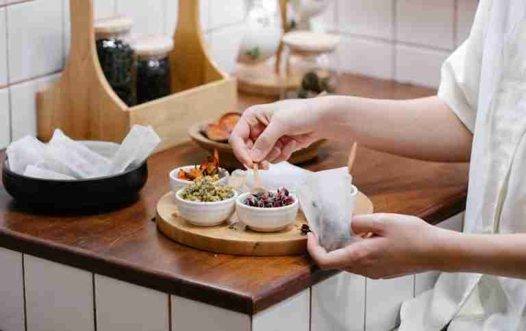 Close-up of hands preparing herbal tea with fresh ingredients in a cozy kitchen.