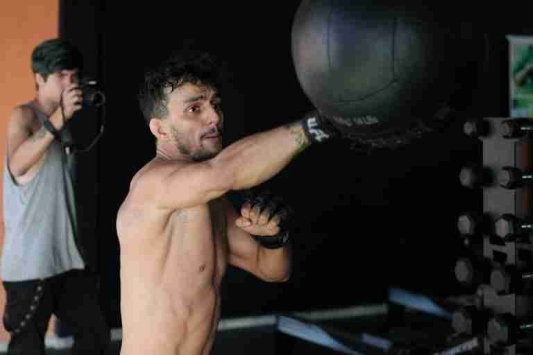 A boxer throws a punch at a heavy bag while training indoors with a camera crew.