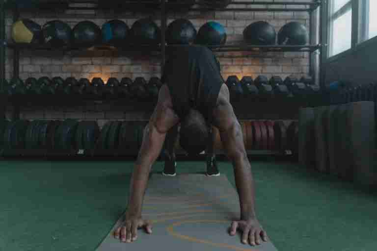 A man performing yoga, doing a downward facing dog pose in a gym environment.