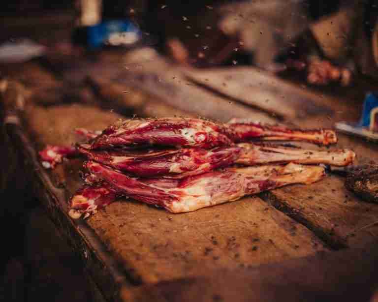 Pile of raw meat on a wooden table surrounded by flies creating a rustic atmosphere.
