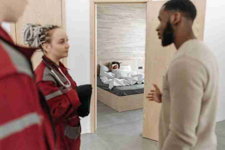 Emergency medical team in discussion while a patient rests in the bedroom.