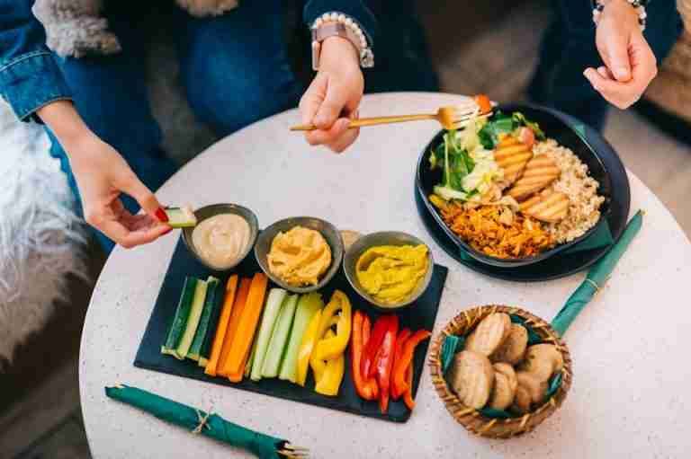 A top-down view of a vibrant vegetable platter with dips beside a quinoa salad bowl.