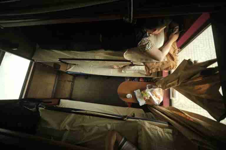 Top view of individuals resting on train bunks with travel essentials.