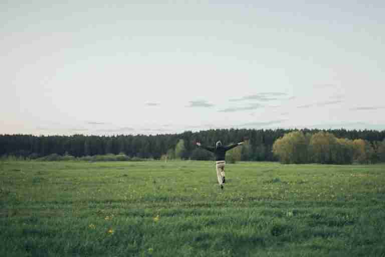 Full length back view of unrecognizable male running towards forest with arms outstretched