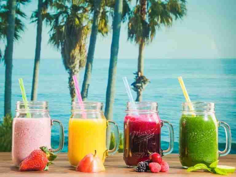 Vibrant smoothies in mason jars with a tropical ocean backdrop, perfect for refreshment.