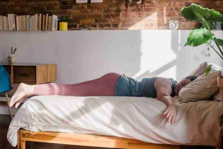 Adult woman in activewear lying on a sunlit bed, exuding calm and comfort in a cozy bedroom setup.