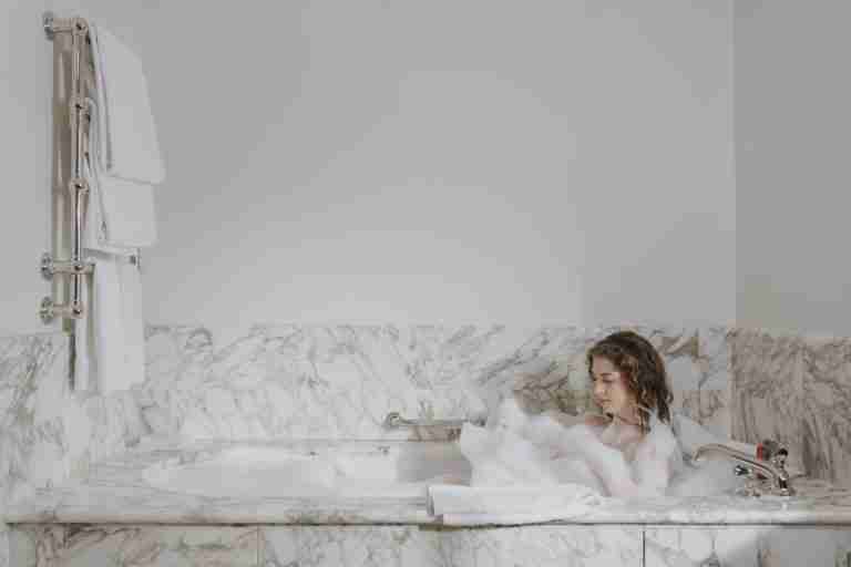 A woman enjoys a calming bubble bath in a luxurious marble bathroom.