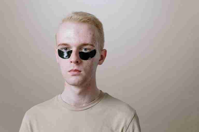 Portrait of a young man wearing under-eye patches, focusing on skincare and self-care routine.