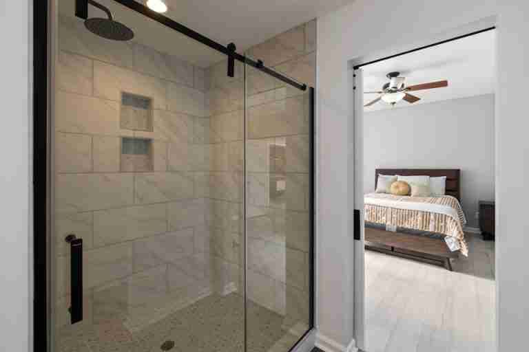 Sleek and modern bathroom with sliding glass shower door adjoining a stylish bedroom.