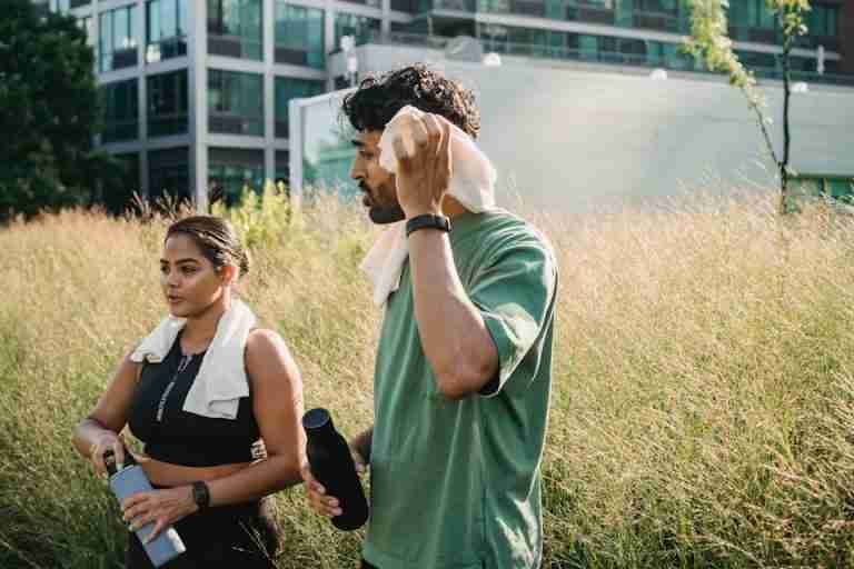 A couple in activewear walk outdoors with water bottles, promoting healthy living and wellness.