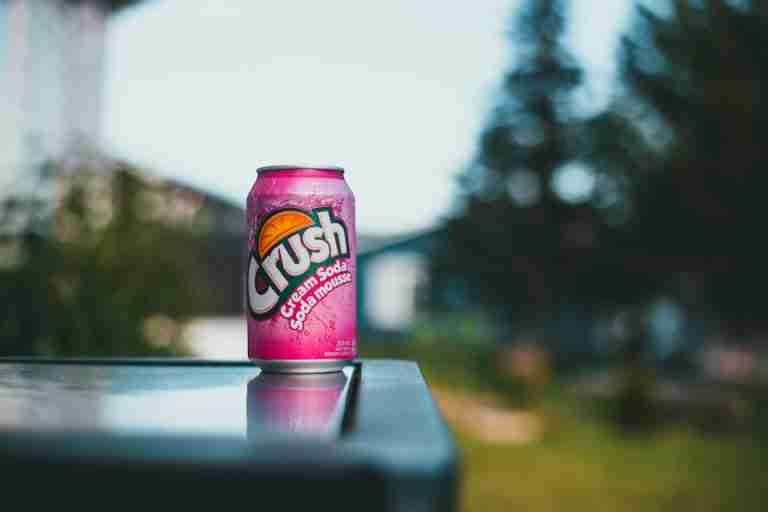 Colorful pink soda can on a reflective table outdoors, perfect for summer vibes.