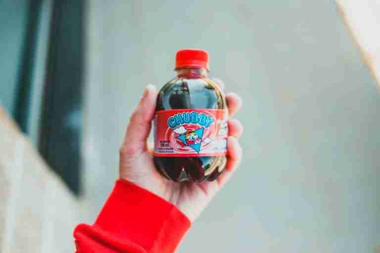 Person holding a Chubby soda bottle with a vibrant red design outdoors.