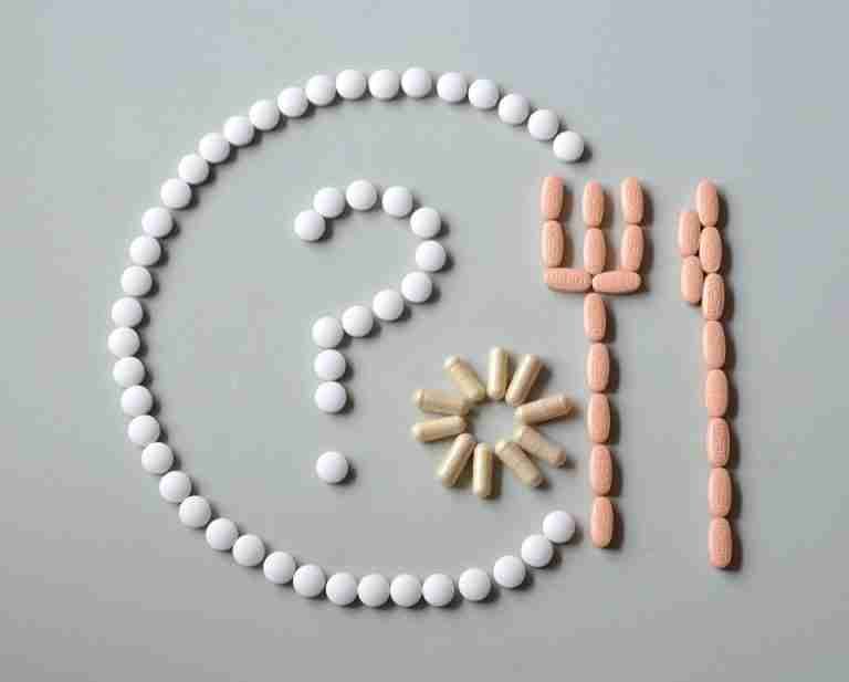 Artistic layout of various pills forming a question mark with fork and sun.