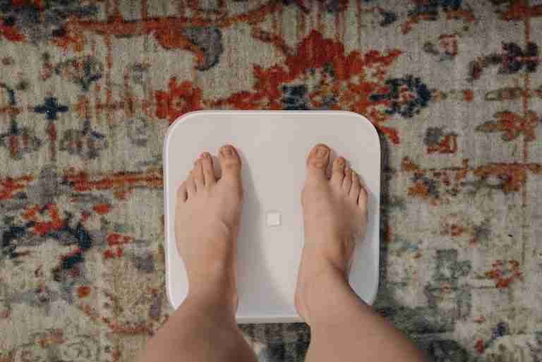 Overhead view of feet on a smart scale atop a decorative carpet, focusing on balance and health.
