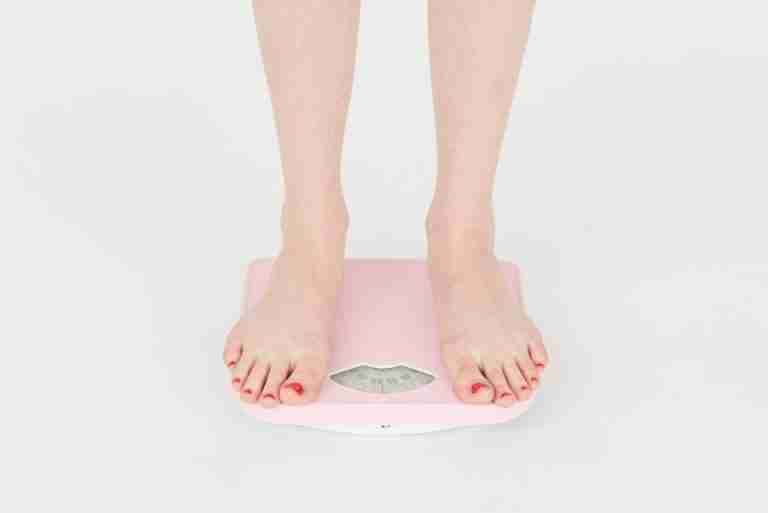 High angle of crop anonymous female measuring weight for control body against white background in studio