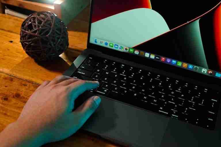 A hand interacting with a laptop on a wooden desk, next to a decorative ball.