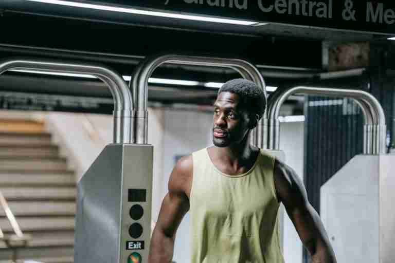 A stylish African American man stands confidently at a subway exit, embodying urban life.