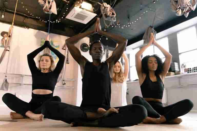 A diverse group of adults meditating in a yoga class indoors, focusing on mindfulness.