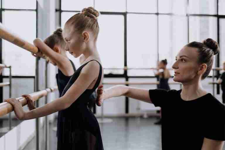 A young ballerina practices ballet with guidance from her instructor in a dance studio.