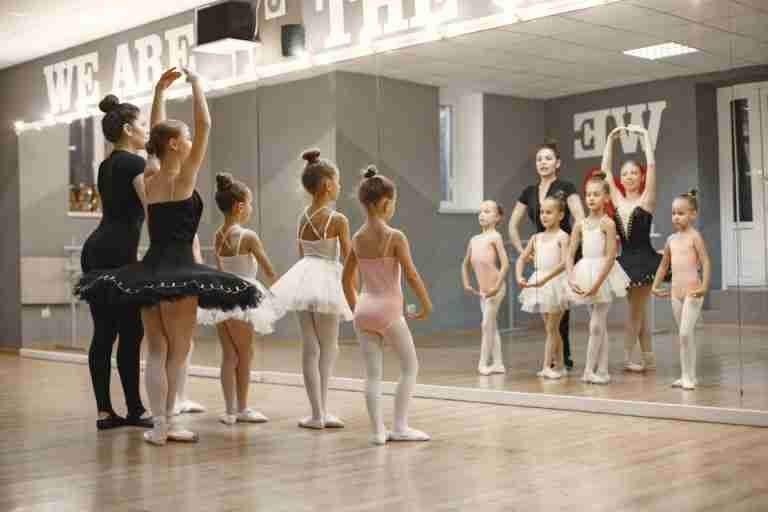 Young ballet dancers practice with their teacher in a studio, reflecting in a large mirror.
