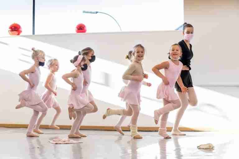 A lively ballet class with young girls in tutus practicing together with an instructor.