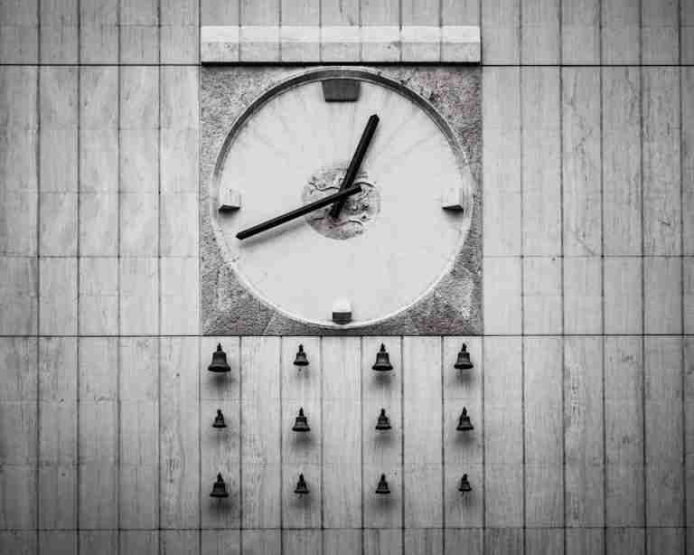 Close-up of a sleek wall clock with bells on a modern architectural facade.