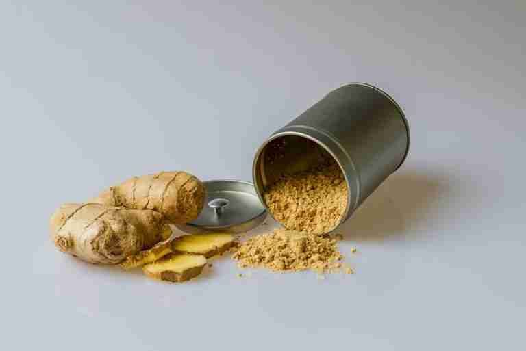Close-up of fresh ginger root with sliced pieces and ginger powder spilled from a metal container.