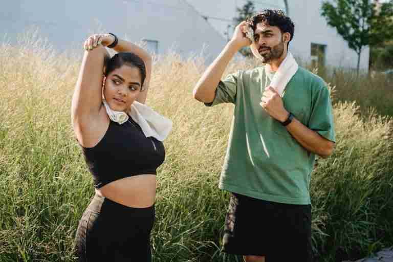 Pair stretching outdoors with towels around necks; fitness and health focus.