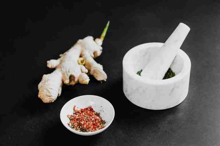 A culinary scene featuring a mortar with spices and ginger root on a black background.