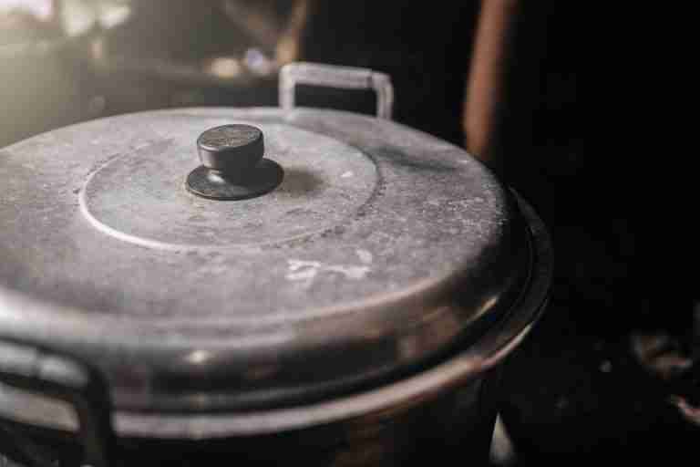 Detailed view of an old metal cooking pot with a black handle in a rustic kitchen setting.