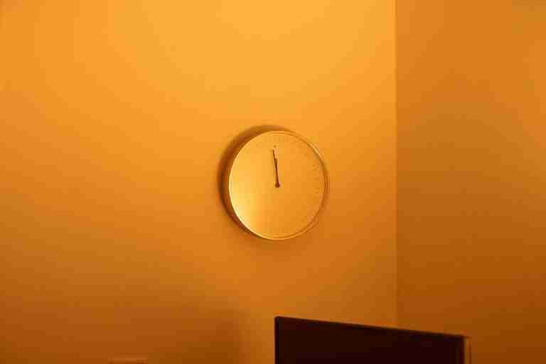 A minimalist wall clock in an orange-hued room with warm lighting, showcasing a simple design.
