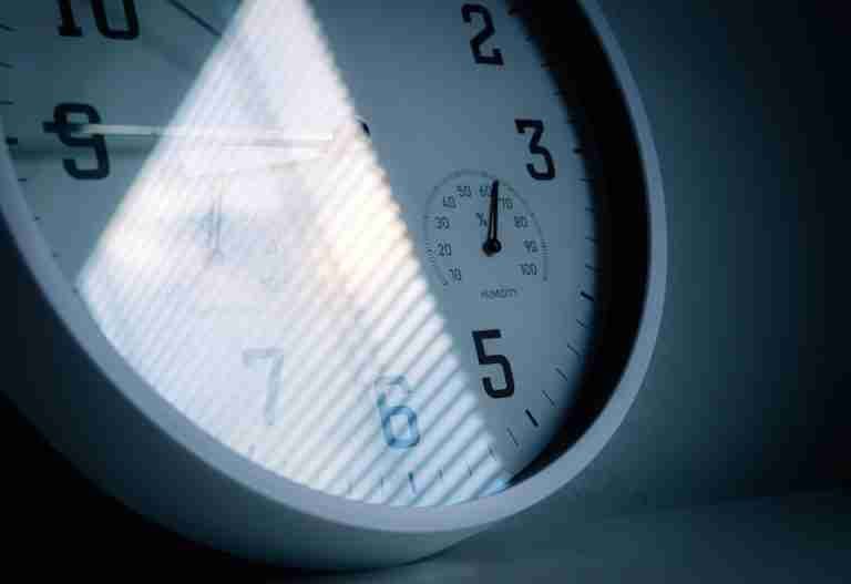 A close-up of a wall clock showing time and humidity, reflecting light and shadows.