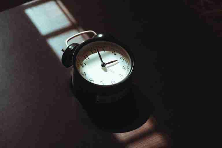 A classic black alarm clock casts shadows in warm morning light, evoking nostalgia.