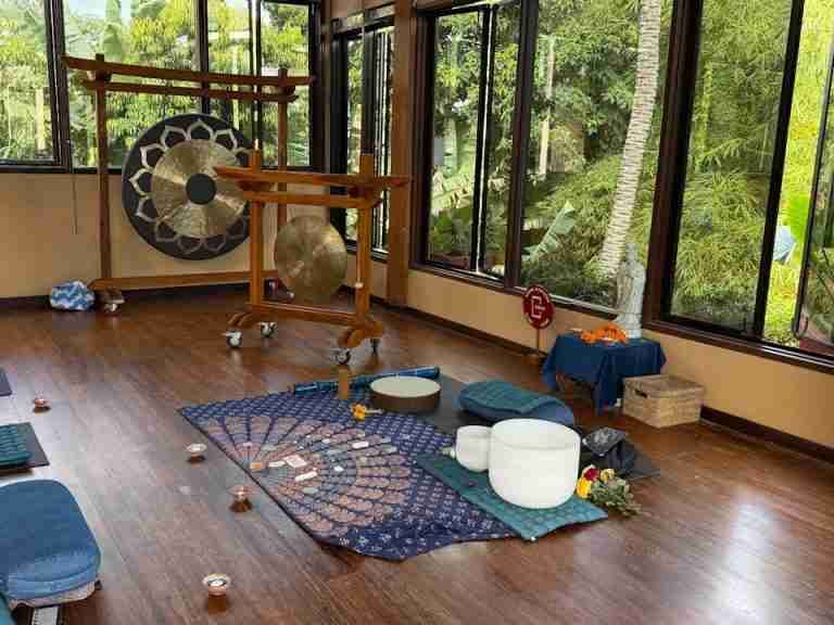 A serene meditation room with gongs, cushions, and mats, set in nature.